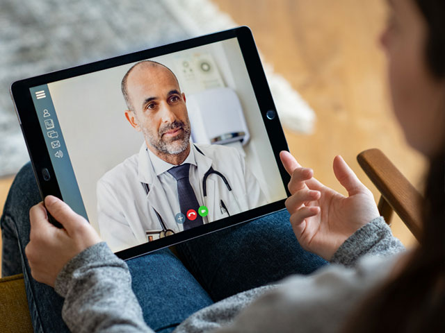 Someone looking at a laptop with a video call from a Doctor on it.